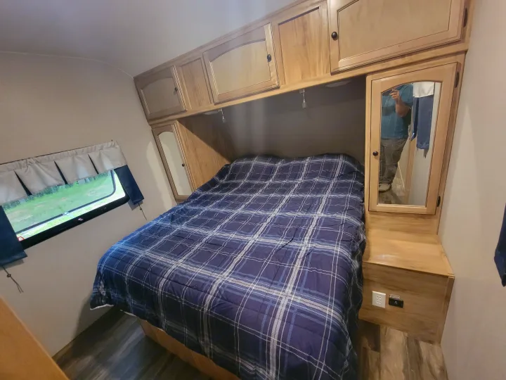 Interior of an RV rental bedroom, featuring a blue plaid bed, wooden cabinets, and a mirrored closet.. Coachmen Freedom Express 323bhds 2019