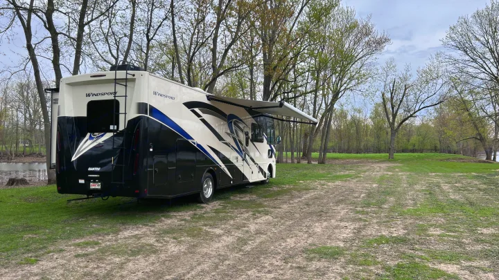 GIANTRV rv rental motorhome parked by the water in a natural, tree-lined setting with its awning extended.. Thor Windsport 2023
