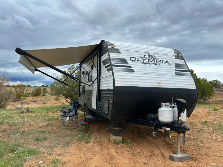 Olympia Sport RV rental travel trailer set up in a sparse, natural landscape with awning extended under a cloudy sky.. Olympia Sport 2022