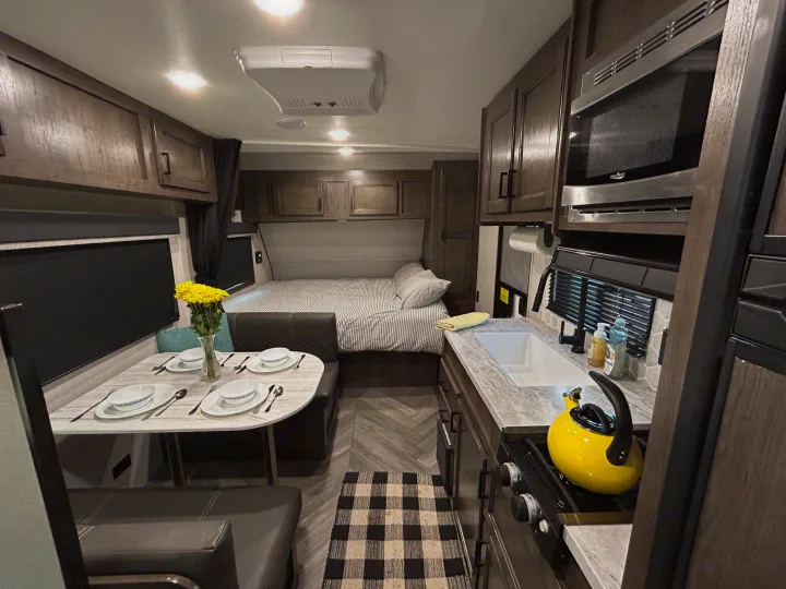 Cozy RV rental interior showcasing a dining area with flowers, a compact kitchen, and a comfortable bedroom. Ready for adventures.. Olympia Sport 2022