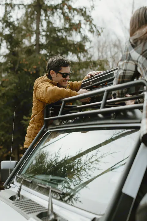 Man loads a rugged vehicle's roof rack with gear, preparing for an RV rental outdoor adventure.. Jeep Wrangler 2023
