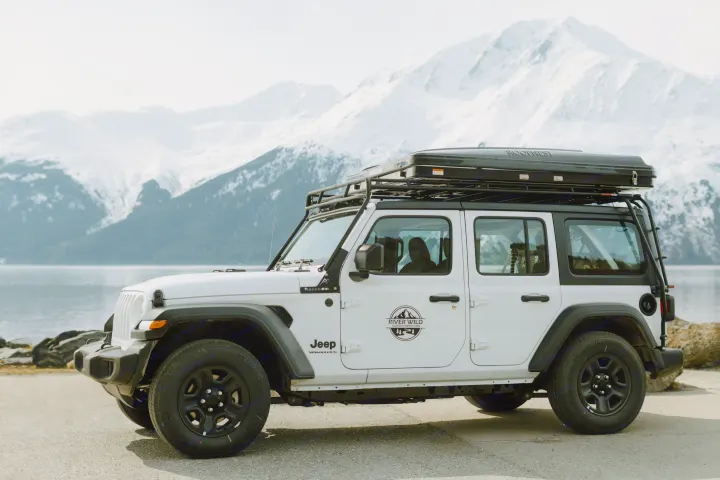 White Jeep Wrangler RV rental with rooftop tent by a snowy mountain lake. Ideal for Alaska adventures.. Jeep Wrangler 2023