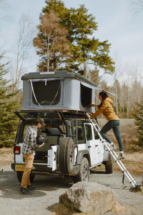 A couple setting up a Roofnest rooftop tent on a white Jeep Wrangler, an ideal rv rental for remote camping and overlanding.. Jeep Wrangler 2023