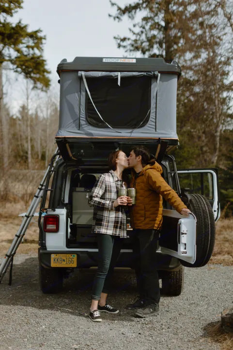 A couple kisses by their white Jeep with a Roofnest rooftop tent. Perfect RV rental for memorable outdoor adventures in Alaska!. Jeep Wrangler 2023