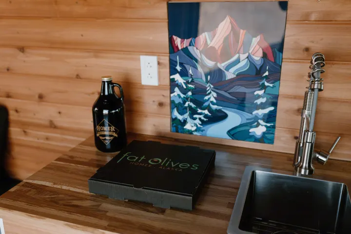 Kitchen counter in an RV rental with local Homer Brewing beer, Fat Olives pizza, sink, and mountain art.. Dodge Ram 2500 (Class B) 2021