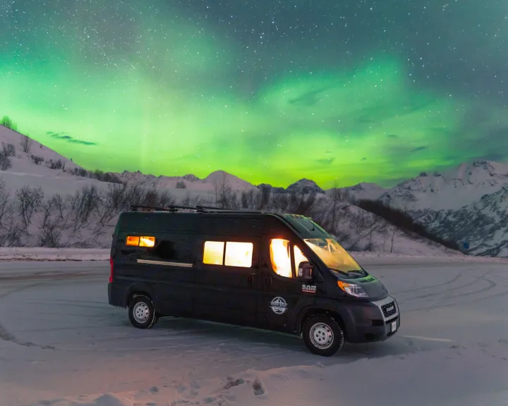 Northern Lights illuminate an RV rental camper van in a snowy Alaskan landscape, ideal for winter adventures.. Dodge Ram 2500 (Class B) 2021