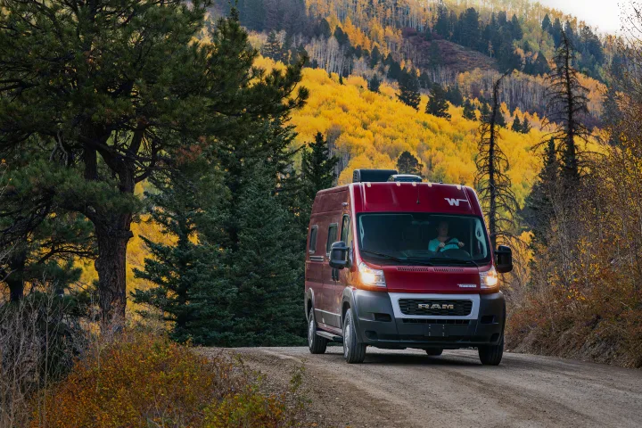Experience fall with an RV rental! A red Winnebago van drives on a dirt mountain road amidst stunning yellow aspen foliage.. Winnebago Solis PX 2023