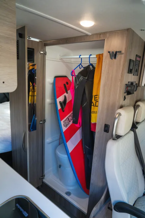 An RV rental's compact interior features a wet bath with a toilet, creatively storing wetsuits, a boogie board, and towels.. Winnebago Solis PX 2023