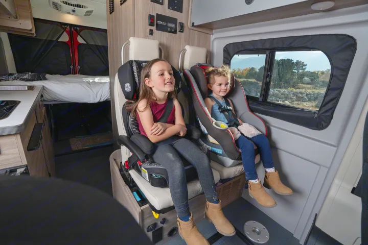 Inside an RV rental: two happy girls safely in car seats in a cozy camper van, ready for a road trip.. Winnebago Solis PX 2023