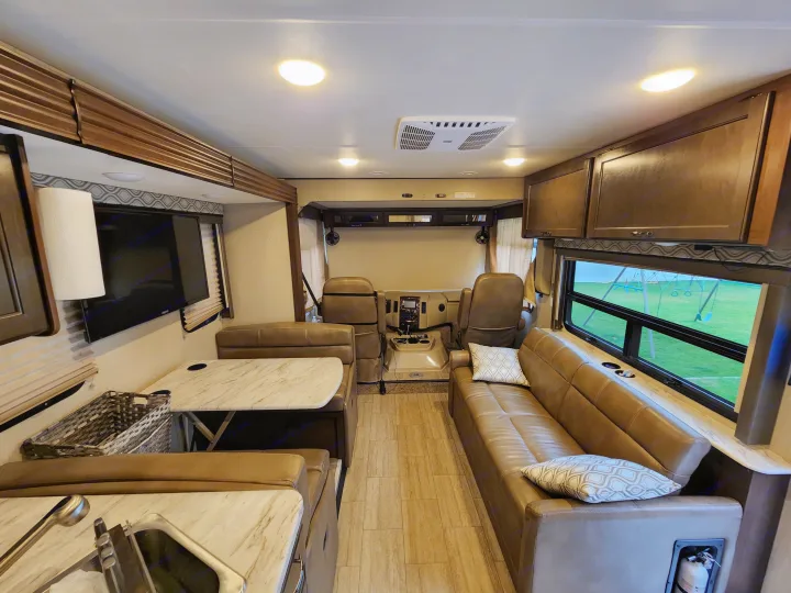 RV rental interior: A bright, modern living space featuring a dinette, sofa, and driver's cockpit, with a playground visible outside.. Thor Freedom Traveler 2020