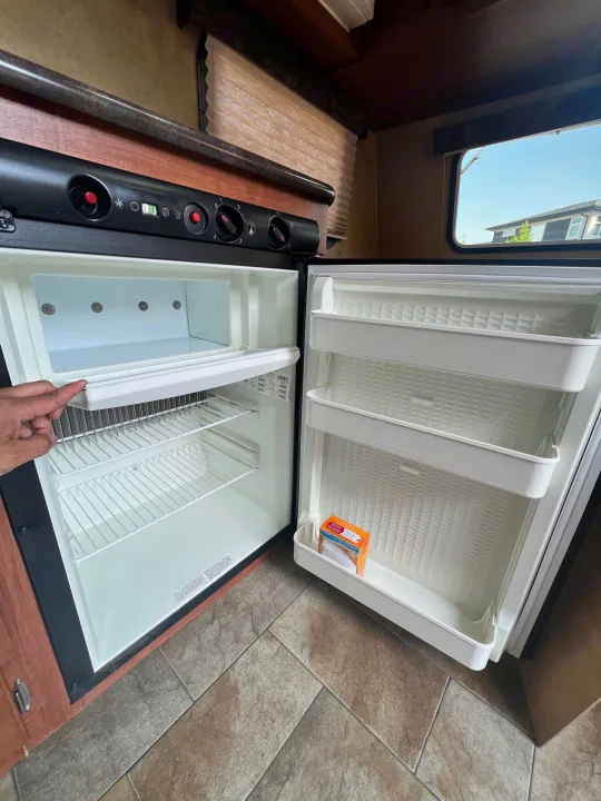 Spacious, empty RV rental refrigerator, open with a hand adjusting a shelf, ready for your road trip groceries.. Jayco Jay Flight Swift 154 BH Slx 2013