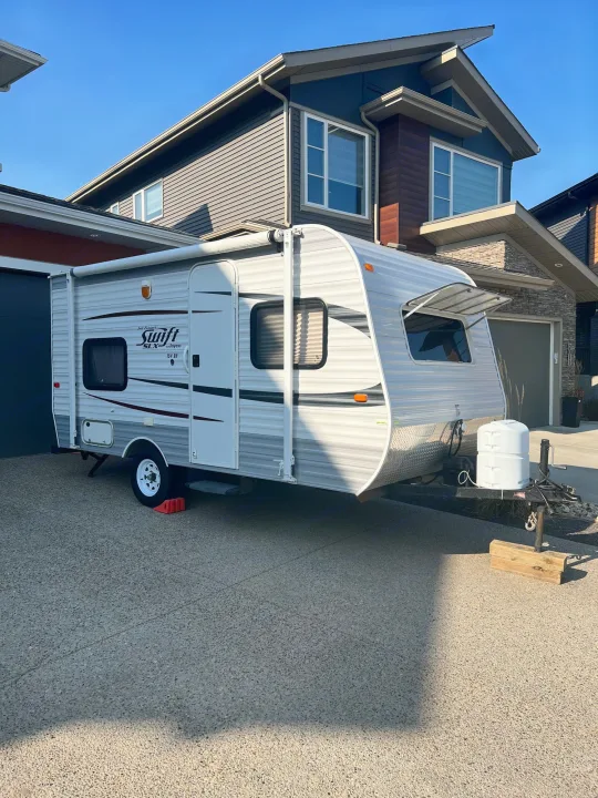 White Jayco Swift RV rental, a travel trailer, parked on a paved driveway in front of modern homes.. Jayco Jay Flight Swift 154 BH Slx 2013