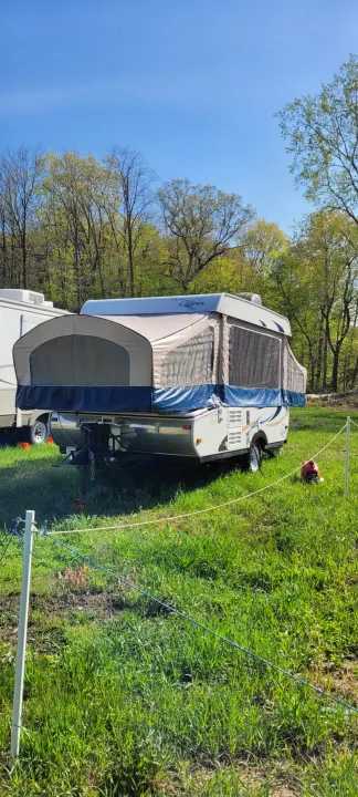 RV rental pop-up camper ready for camping in a sunny, tree-lined field under a blue sky.. Coleman clipper 2011