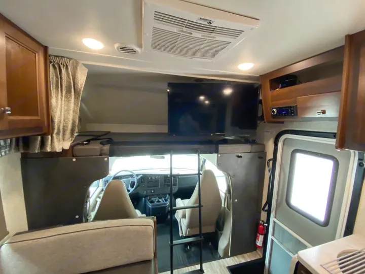 Spacious RV rental interior featuring a cab-over bunk with TV, cockpit, kitchen, and entry door. Ideal for road trips!. Forest River Sunseeker 2019