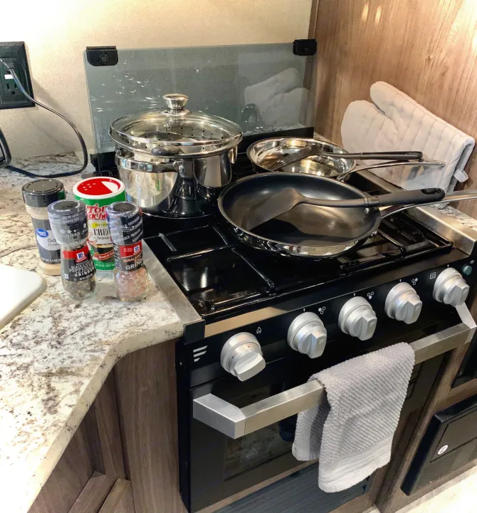 Prepare meals easily in your RV rental! This compact kitchen features a stovetop, pots, pans, and spices ready for cooking.. Keystone RV Hideout LHS 2019