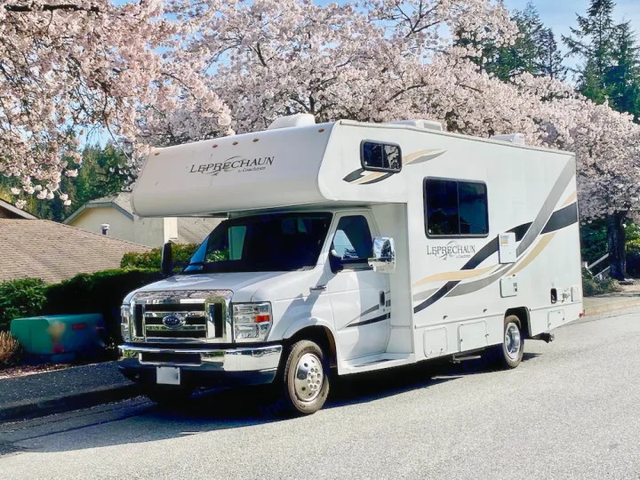 A white Coachmen Leprechaun Class C motorhome RV rental parked under blooming cherry blossom trees, ready for spring adventures.. Forest River Coachmen Leprechaun 2014