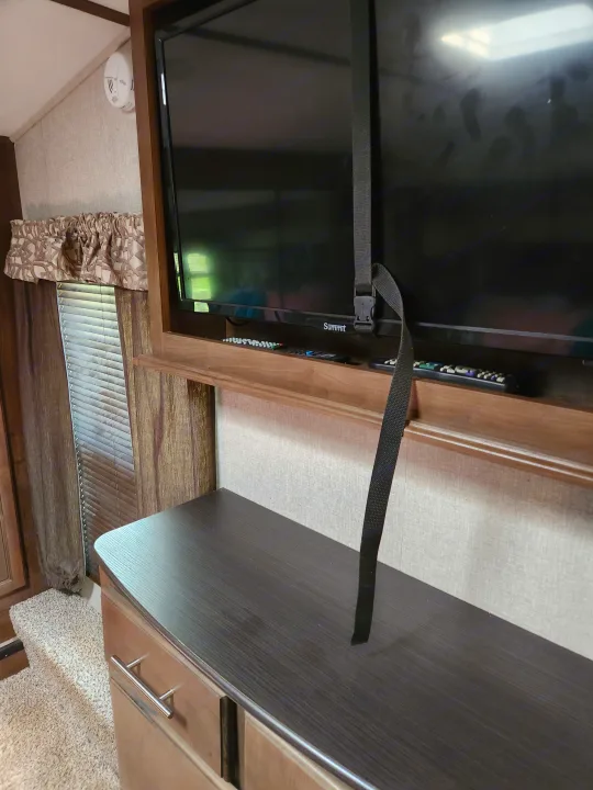 RV rental interior with a secured TV, remote control, and ceiling-mounted smoke detector for travel safety.. Keystone RV Cougar 2019