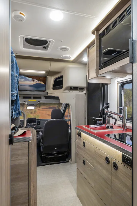 Inside this rv rental: a well-equipped kitchen with microwave, sink, and TV area near the driver's cabin for travel comfort.. Winnebago EKKO POP TOP 2027