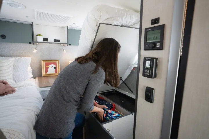 Efficient RV rental interior: Woman accesses spacious under-bed storage for belongings in this compact, organized space.. Winnebago EKKO POP TOP 2027