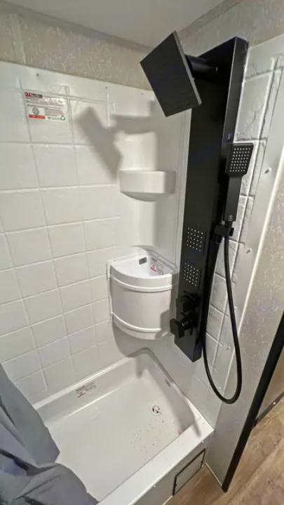 RV rental shower: modern black panel, rainfall & handheld heads, body jets, white tiled walls & shelves.. Forest River Cherokee Wolf Pup Black Label 2022