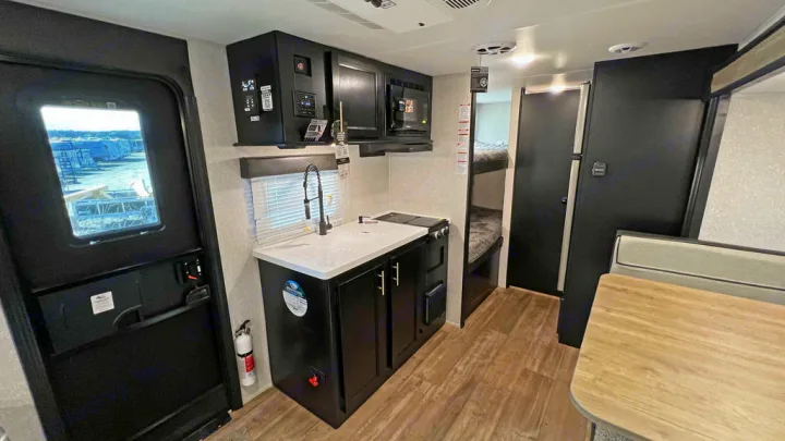 Inside this RV rental: a compact kitchen with sink/stove, microwave, fridge, bunk beds, and dining area, ideal for trips.. Forest River Cherokee Wolf Pup Black Label 2022