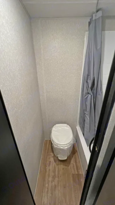 Compact RV rental bathroom, featuring a clean toilet and shower with a gray curtain.. Forest River Cherokee Wolf Pup Black Label 2022