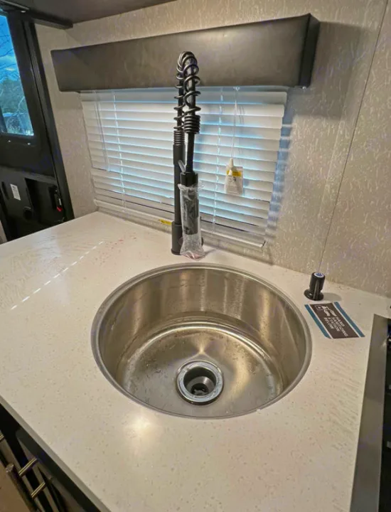 Inside an RV rental: a clean, modern kitchen area with a stainless steel sink, black spring faucet, and light countertop.. Forest River Cherokee Wolf Pup Black Label 2022