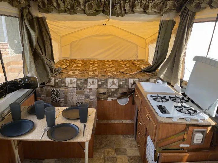 Cozy pop-up rv rental interior featuring a bed, dining table with place settings, and a compact kitchen. Ready for your adventure!. Forest River Rockwood Premier 2009
