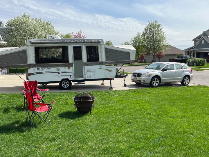 A pop-up camper (RV rental) fully set up on a driveway, with a silver car, red chairs, and fire pit on the lawn.. Forest River Rockwood Premier 2009