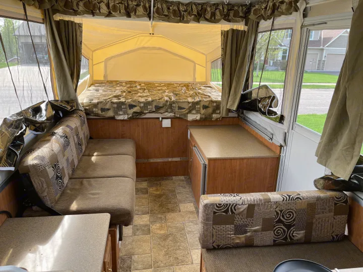 Inside an RV rental: a cozy pop-up camper interior with a patterned bed, seating area, and counter space.. Forest River Rockwood Premier 2009