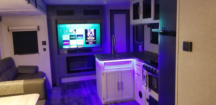 Modern RV rental interior with purple LED mood lighting, featuring a cozy living area, TV, electric fireplace, and kitchen.. Crossroads RV Volante 2022