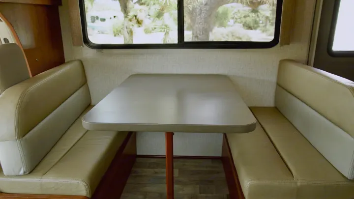 RV rental dinette: comfy tan banquette seating, table, and a clear window view of nature outside.. Winnebago Minnie Winnie 2017