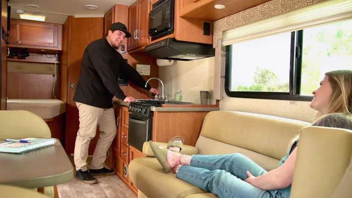 Homey RV rental interior: a man at the kitchen sink, a woman relaxes on comfortable seating.. Winnebago Minnie Winnie 2017