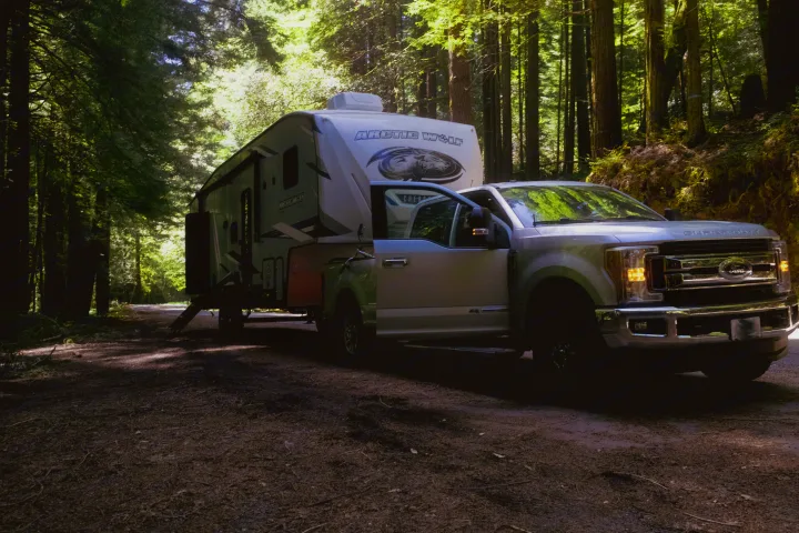 Explore nature with this RV rental: A Ford Super Duty truck and Arctic Wolf travel trailer parked on a sunlit forest road.. Forest River Cherokee Arctic Wolf 2022