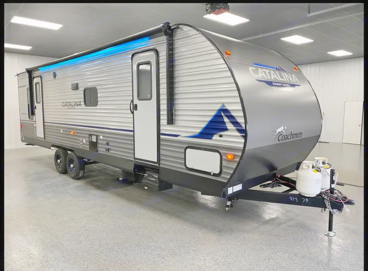 This gray Coachmen Catalina travel trailer, a great RV rental option, features blue awning lights and front propane tanks.. Coachmen Catalina 2023