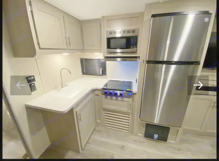 RV rental kitchen featuring stainless steel fridge, microwave, stovetop, sink, and light gray cabinets. Modern interior.. Coachmen Catalina 2023