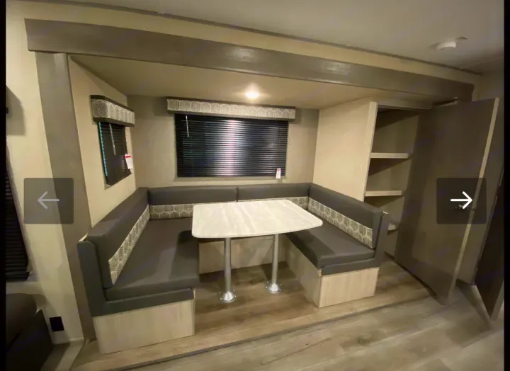 RV rental interior: modern dinette with U-shaped dark gray seating, light table, windows, and built-in storage.. Coachmen Catalina 2023