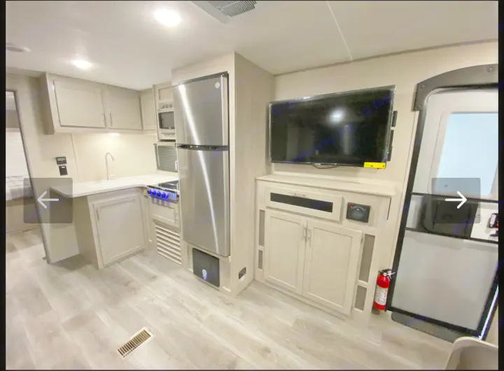 Modern RV rental interior: kitchen with stainless steel appliances, TV, and light wood flooring by the entrance.. Coachmen Catalina 2023