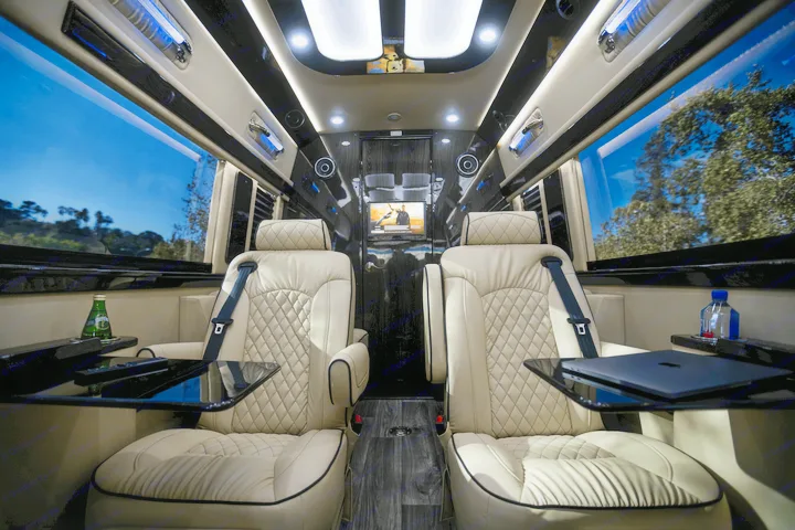 Plush interior of a luxury RV rental. Features comfortable captain's chairs, personal tables, a monitor, and scenic window views.. Ultimate Toys Ultimate Coach 2023