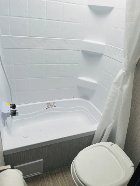 Compact RV rental bathroom: clean tub/shower with built-in shelves, toilet, and wood-look floor.. Palomino PUMA 22RBC 2022