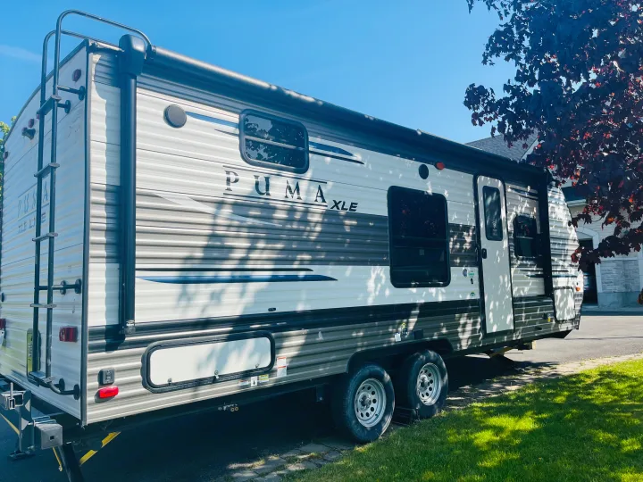 A Puma XLE travel trailer, a common type of RV rental, is shown parked on a grassy area under clear skies.. Palomino PUMA 22RBC 2022