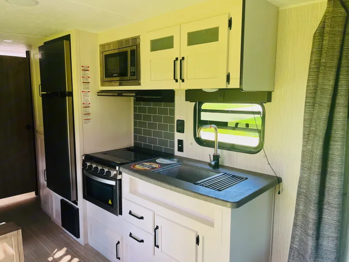 Explore this clean, modern RV rental kitchen featuring a refrigerator, microwave, oven/stove, sink, and bright white cabinets.. Palomino PUMA 22RBC 2022