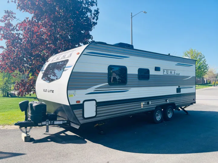 A sleek Puma XLE Lite travel trailer, white and grey with blue accents, awaits its next RV rental adventure.. Palomino PUMA 22RBC 2022