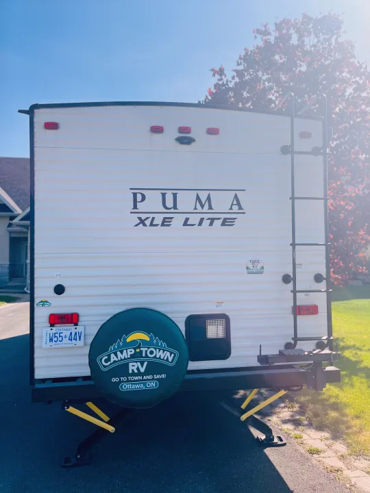 Back of a Puma XLE Lite travel trailer, an excellent rv rental option, with an Ontario license plate and Camp Town RV spare tire cover.. Palomino PUMA 22RBC 2022