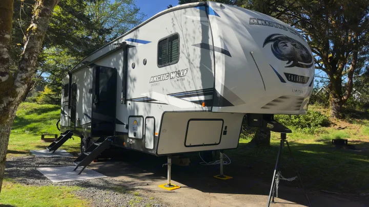 An Arctic Wolf fifth-wheel RV rental is set up at a sunny campsite with trees and grass, ready for adventure.. Forest River Cherokee Arctic Wolf 2022