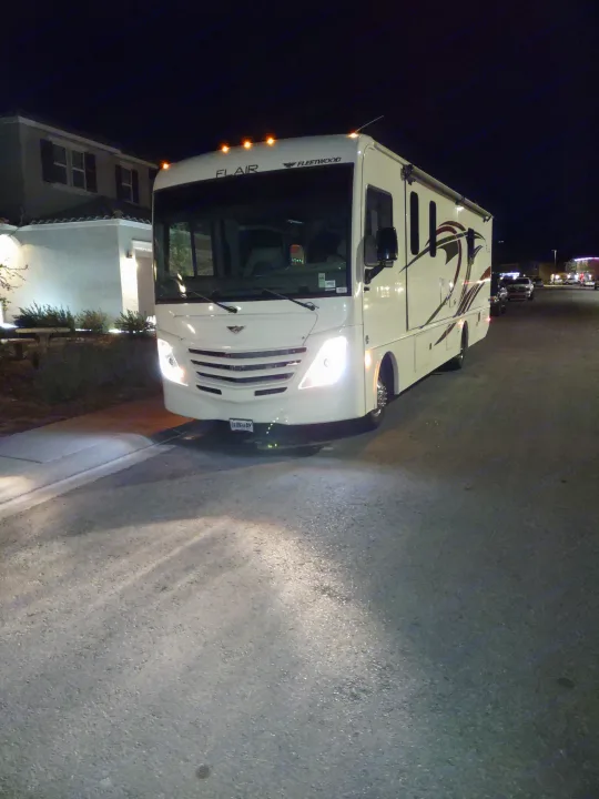 RV rental: A large white Fleetwood Flair motorhome parked at night, its headlights illuminating the dark street.. Flair-Fleetwood Flair-Fleetwood Motorhome 2020