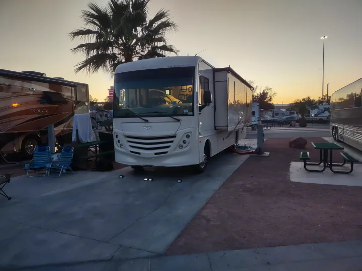 Spacious RV rental set up at a tranquil RV campsite. Features a picnic area and palm trees under a soft, evening sky.. Flair-Fleetwood Flair-Fleetwood Motorhome 2020