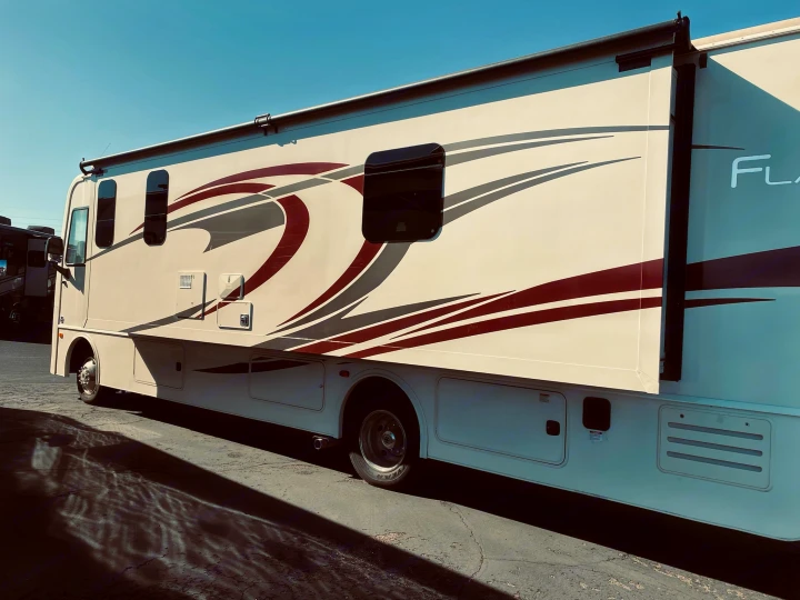Explore with this cream-colored RV rental, featuring striking red/gray graphics & an extended slide-out, under a clear sky.. Flair-Fleetwood Flair-Fleetwood Motorhome 2020