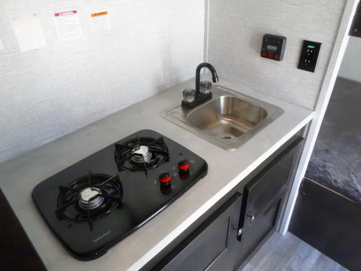 An RV rental's compact galley featuring a two-burner stove, sink, and cabinetry. Perfect for on-the-go meals.. Braxton Creek Bushwhacker Plus 2022