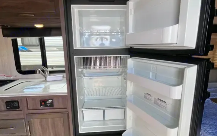 Bright, empty refrigerator in a modern RV rental kitchen with sink and counter.. Genesis Supreme Rv Genesis Supreme 2021